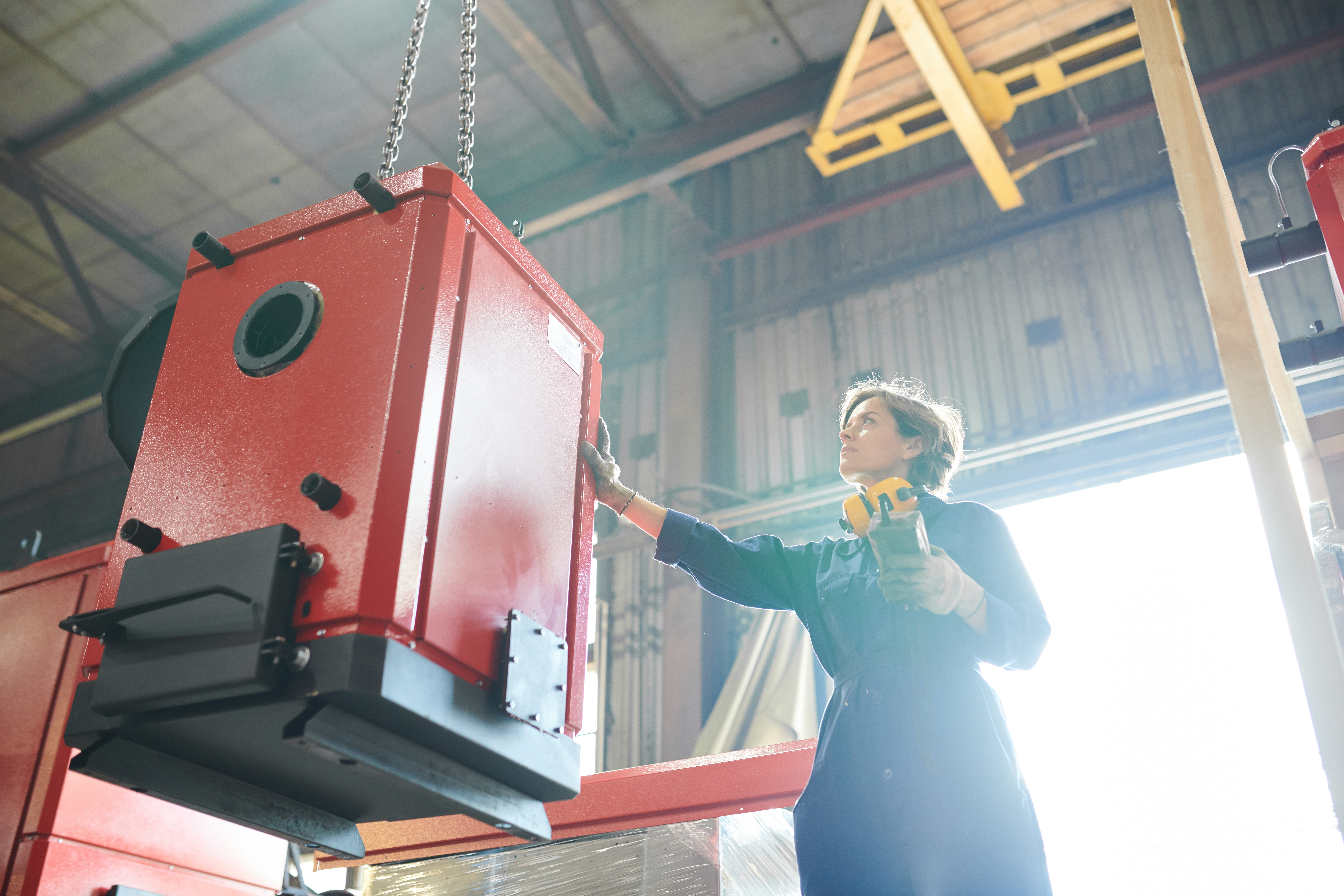 Low angle portrait of female worker moving giant metal parts at plant, copy space